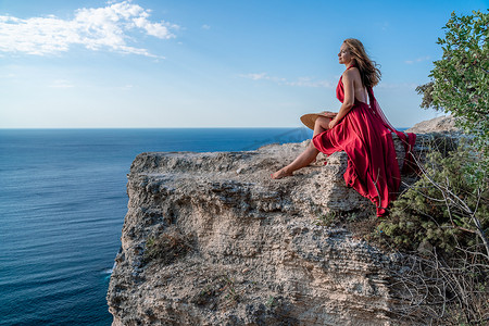 一个穿着红色长裙、头发飘逸的女孩坐在海上的一块岩石上。
