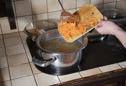 一个女人把磨碎的胡萝卜放入锅中，这是煮罗宋汤的原料