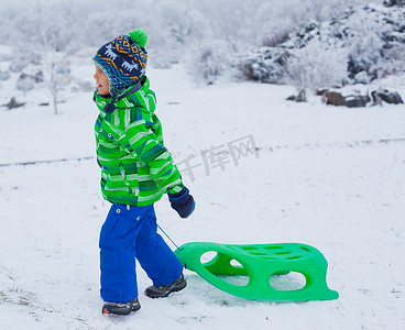 小男孩在冬季公园玩雪橇
