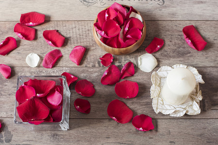 玻璃花瓶和木弓，里面装满了红色玫瑰花瓣，白色芳香香草蜡烛。