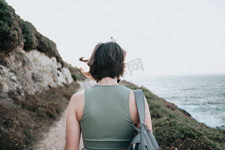 旅行背影摄影照片_年轻的嬉皮士女孩在岸上徒步旅行时背影，旅行和低预算旅行概念，复制空间。