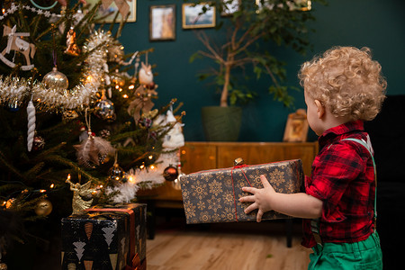 圣诞节气氛摄影照片_圣诞节那天，一个两岁的小男孩拿着一个礼物包。