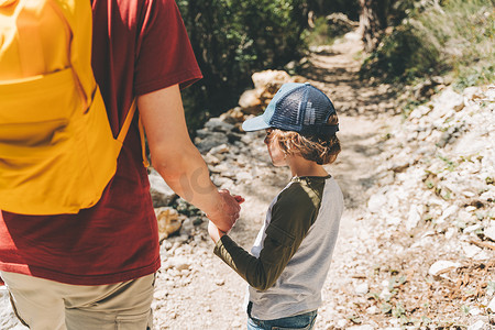 游客小学生和他爸爸在春天森林里走石头小径的特写镜头后视图。