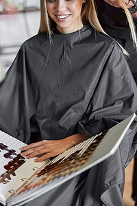 金发女客户正在选择书中的颜色，而美发师正在剪头发
