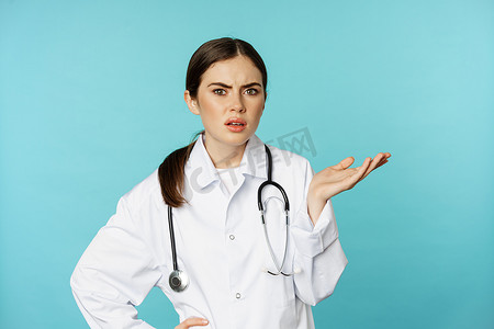 恼怒、疲惫的女医生的画像，脸掌，沮丧的翻白眼，被愚蠢的东西困扰，穿着白大衣站在绿松石背景上