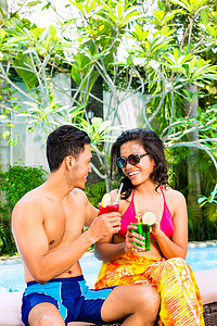 亚洲比基尼摄影照片_亚洲夫妇在游泳池喝鸡尾酒