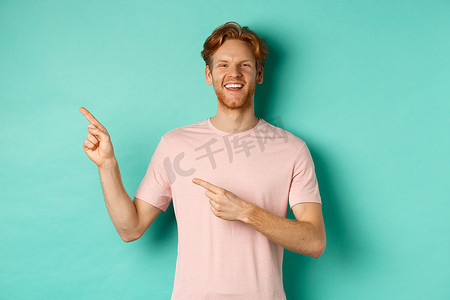 身穿 T 恤的帅气白人男子向左指指点点，笑着开心，展示广告，站在绿松石色背景上
