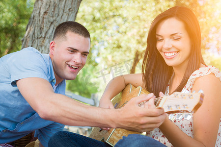 英俊的年轻人在公园教混血女孩弹吉他。