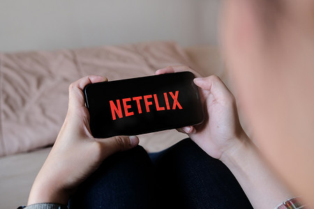 泰国清迈，2020 年 3 月 29 日：女性在家中手持带有 Netflix 标志的智能手机在苹果 iPhone Xs 上。