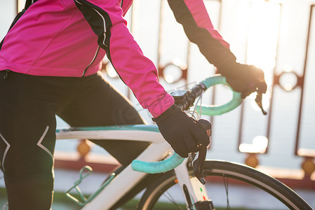 在寒冷阳光明媚的秋日，在公路自行车车把上戴手套的女骑车人手的特写照片。