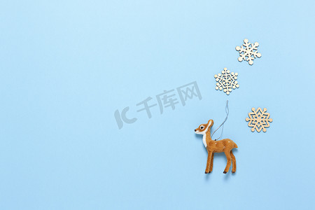 圣诞装饰、自然主义玩具狍子和柔和的蓝色背景上的三片小木雪花，复制空间。