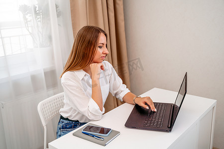 欧洲职业女性坐在家庭办公室的桌子旁，手里拿着一台笔记本电脑，一位积极的女性一边在 PC 上工作一边学习。