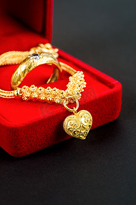金色的装饰摄影照片_黑色红色天鹅绒盒中的金项链和心形吊坠和金戒指。