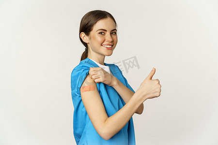 微笑的护士，穿着磨砂膏的医生，医务人员用贴片展示她接种过疫苗的肩膀，竖起大拇指，建议接种冠状病毒疫苗，白色背景