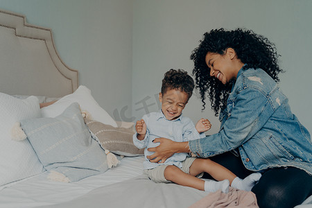 黑人脏辫摄影照片_慈爱的美国黑人母亲在卧室里一起玩乐时挠痒痒的儿子