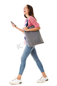 在孤立的白色背景下，带着钱包和智能手机行走的时尚年轻亚洲女性的侧面肖像