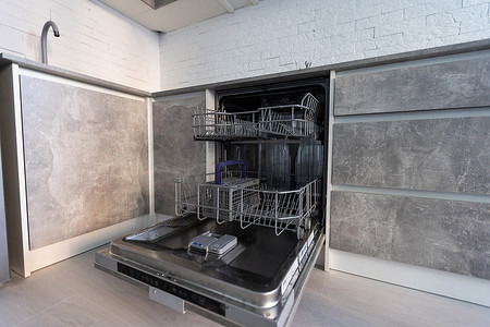 现代厨房配有带开门的空内置洗碗机、不锈钢台下式厨房水槽和自来水、黑色电磁炉、安装在白色台面上的炊具。