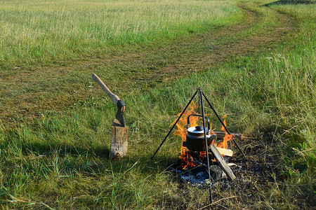 水壶摄影照片_带篝火、水壶和钢坯斧头的徒步景观。
