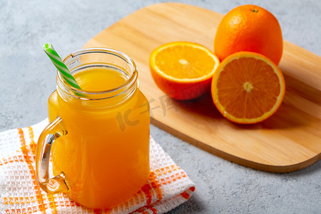 果汁吸管摄影照片_用橙子新鲜制作的柑橘汁，装在罐子杯里，灰桌上放着吸管
