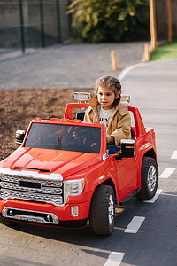 可爱的小女孩骑着一辆红色的电动吉普车在迷你城市中行驶。