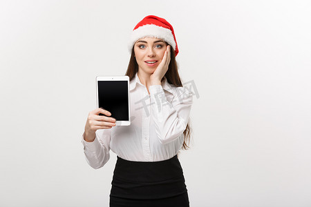 经营理念-年轻的白人女商人在圣诞节主题中展示带有令人惊讶的面部表情的数字平板电脑。