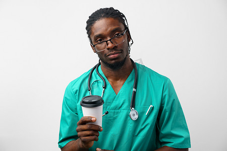疲惫背景摄影照片_疲惫的非洲裔美国男医生在白色背景下拿着一杯咖啡