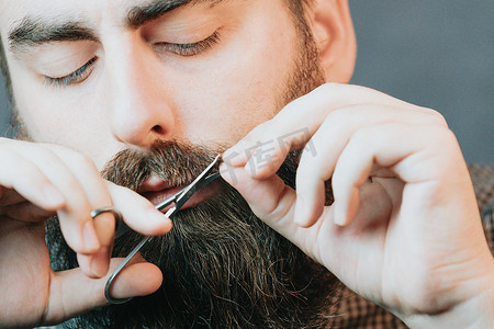留胡子的帅哥剃胡子，年轻的白种人留胡子的男人在隔离期间在家里修剪胡须。