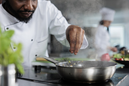 大厨穿着烹饪制服在餐厅厨房用新鲜切碎的香草装饰美食。
