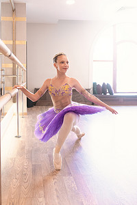 一个在芭蕾课上穿着足尖鞋微笑的少女的特写，她靠近一个框架和大镜子做运动和伸展运动