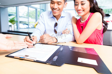汽车融资摄影照片_亚洲夫妇在经销商处签订汽车销售合同