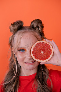 甜美快乐的黑发女人女孩，在橙色背景下，在靠近皮肤的脸上切下葡萄柚片。