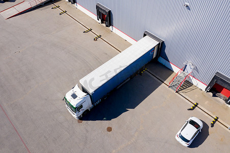 卡车与附加半拖车离开工业仓库/仓储大楼/装货区的空中拍摄，许多卡车正在装卸商品