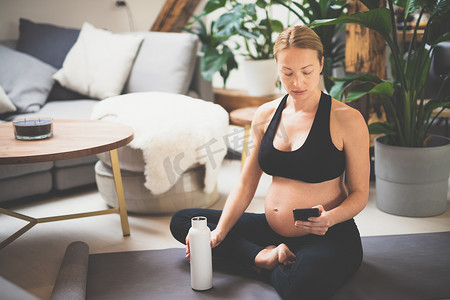 年轻快乐开朗的美丽孕妇在家庭健康锻炼计划后休息、补水、喝瓶中的水。