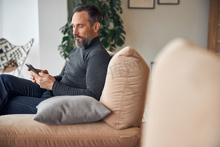 在现代舒适的办公室休息区，白人成年男子正与智能手机坐在一起