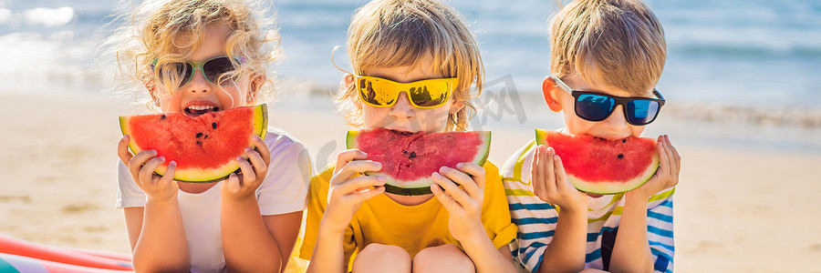 孩子们戴着太阳镜在海滩上吃西瓜横幅，长格式