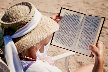 戴着帽子在海滩上阅读印刷书籍的成年女性