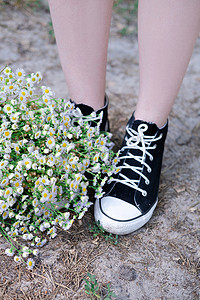 夏季，在自然背景下，运动鞋附近无法辨认的女性腿和户外的白色野花