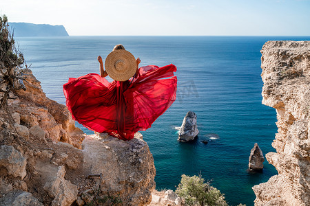 身着飘扬红裙、头戴草帽的女子，映衬在大海的映衬下。