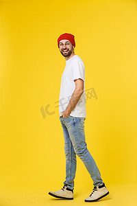 背带裤小熊摄影照片_年轻的时髦男人戴着帽子，背带裤，在黄色背景上隔离。