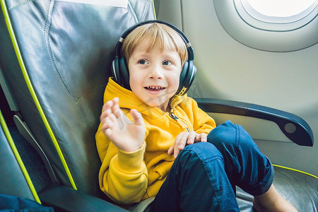戴耳机的男孩摄影照片_戴耳机的男孩在飞机上观看和收听飞行娱乐节目