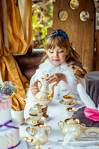 爱丽丝梦游仙境中一个美丽的小女孩在桌上把茶倒进杯子里的前视图