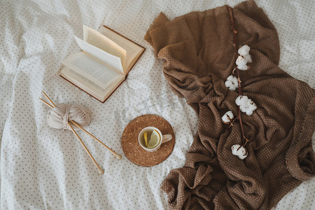 舒适的冬季背景，配有书、茶杯和织针，位于温暖柔软的床顶视图中。
