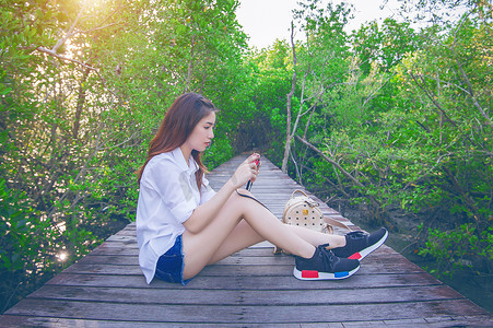 女孩独自坐在木桥上，手拿相机。