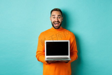 穿着橙色毛衣、留着胡子的帅哥展示笔记本电脑屏幕，展示促销，站在浅蓝色背景上
