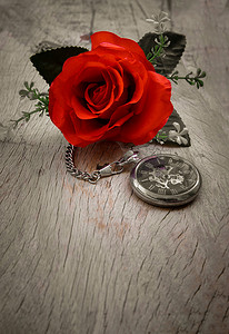 红玫瑰花和旧木板背景上的一块复古怀表。