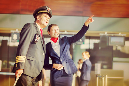 年轻漂亮的空姐在机场与飞行员一起指着飞机