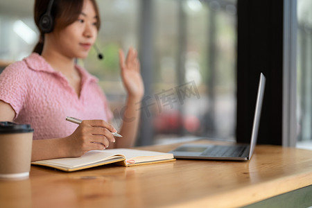 亚洲年轻女性在家听在线网络研讨会时做笔记，戴着耳机，使用笔记本电脑学习外语，电子学习概念，隔离期间待在家里