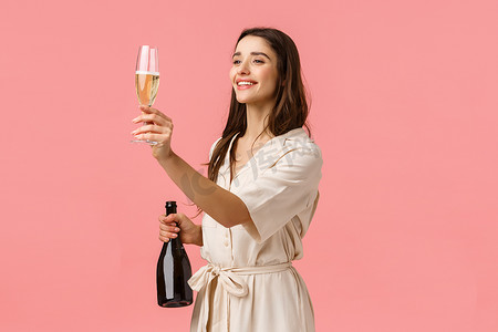女孩为朋友举杯，敬酒，看着左边的人，拿着香槟，开心地微笑，站在粉红色的背景下，庆祝特殊的日子