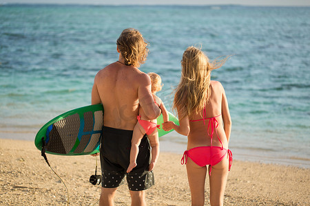 体育家庭爸爸、妈妈和女儿在沙滩上散步。