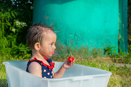 一个穿着泳装坐在浴缸里吃成熟草莓的小女孩